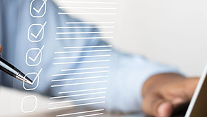 A person holding a pen checks off items on a transparent digital checklist, with a laptop visible in the background. The scene suggests productivity or task management.