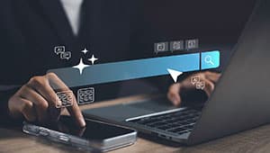 Person using a laptop and smartphone at a desk, with a digital search bar and icons for messages and social media overlayed, symbolizing internet searching and online communication.