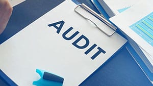 A clipboard with the word AUDIT written on a sheet, next to a blue highlighter and stacked documents with charts—a perfect setup for evaluating site performance or even determining how many WordPress plugins is too many for optimal website efficiency.