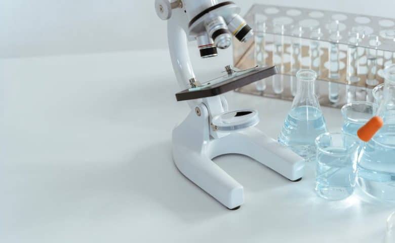 Microscope and glass lab beakers on a white laboratory bench