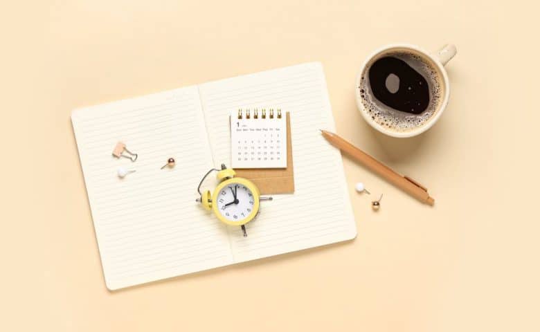 Open notebook with an alarm clock, desk calendar, pen, and coffee