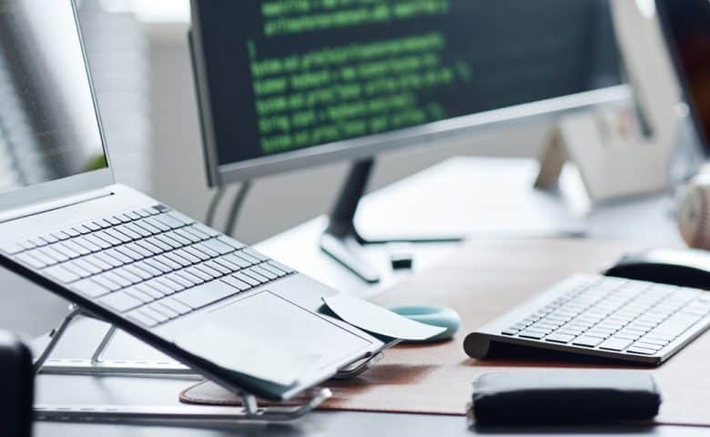 Developer desk with a laptop, keyboard, and monitor showing code